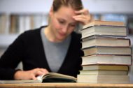 A student is sitting in a library with a stack of books; she is researching for her literature review.